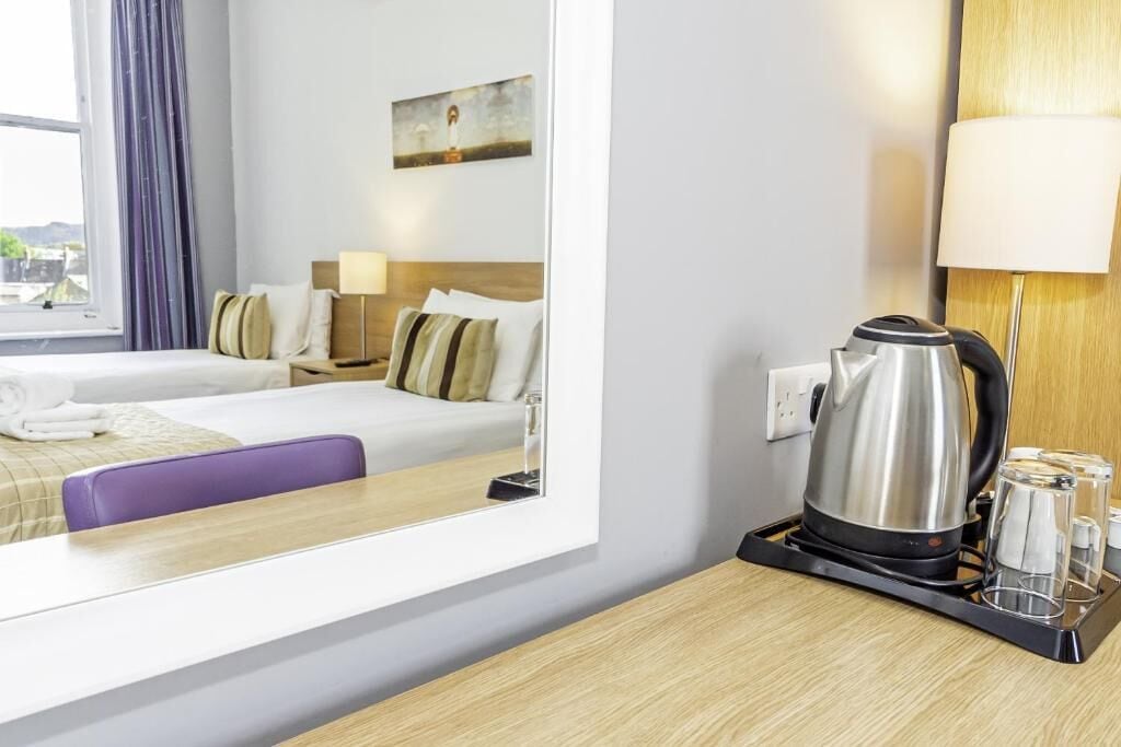 Ein Hotelzimmer mit einem Bett, einem Schreibtisch mit Wasserkocher und einem Fenster mit Vorhängen.
