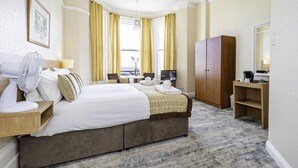Une chambre d’hôtel comprenant un lit, un bureau, une chaise, une armoire et une grande fenêtre avec des rideaux.