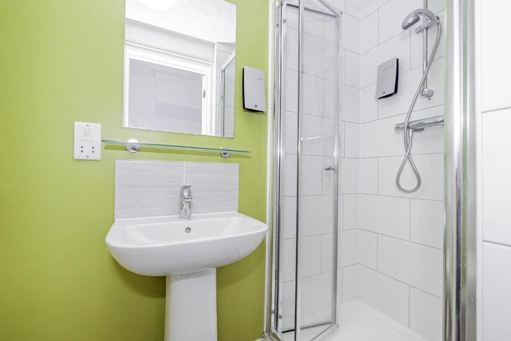 A bathroom with a white sink, a glass shower enclosure, and a green wall.