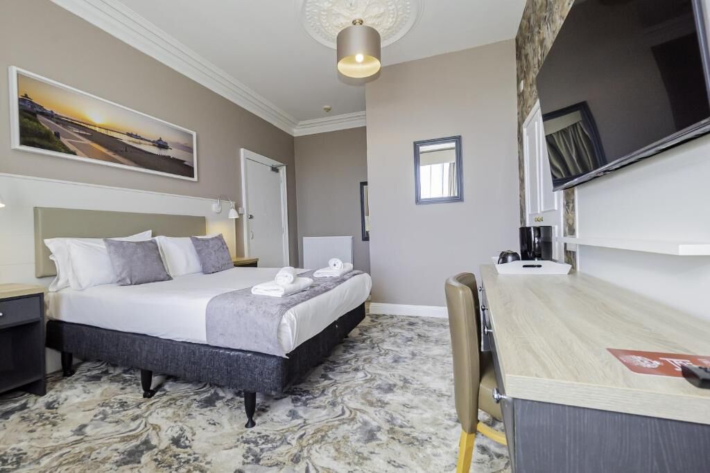 A hotel room with a bed, a desk, a chair, a television, and a painting on the wall.