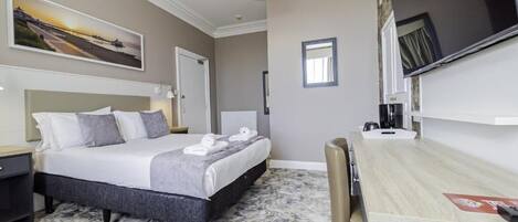 A hotel room with a bed, a desk, a chair, a television, and a painting on the wall.