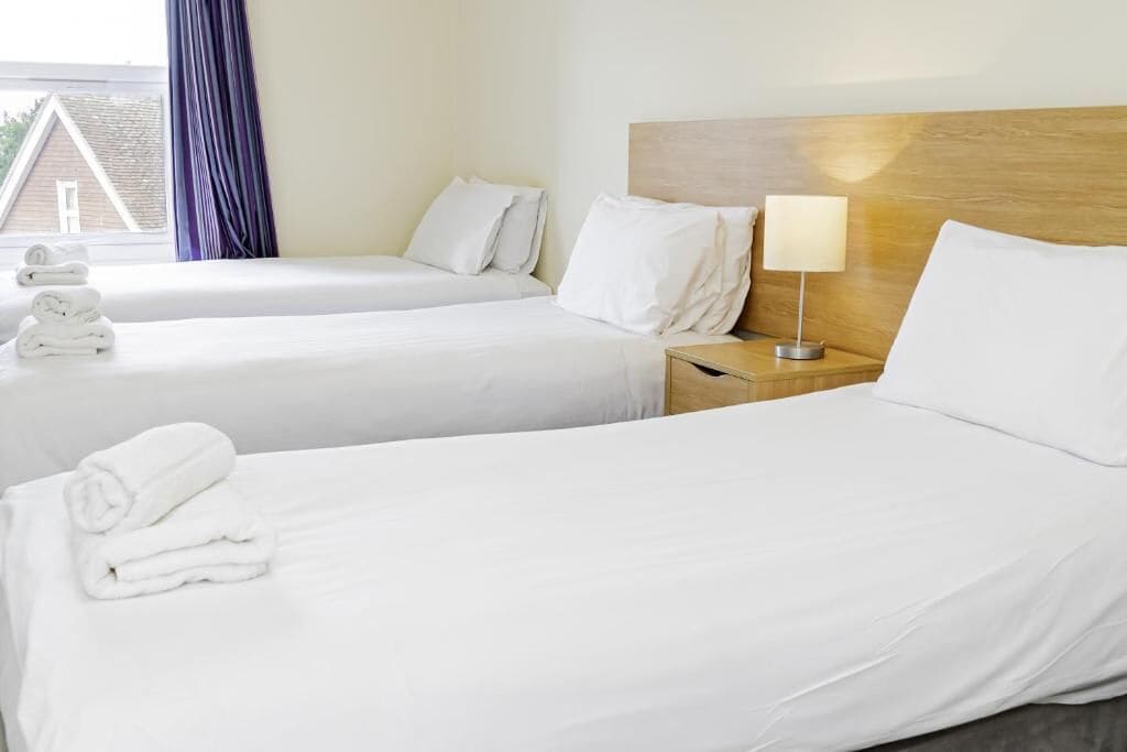 A hotel room with two beds, a wooden headboard, a bedside lamp, and neatly folded towels on each bed.