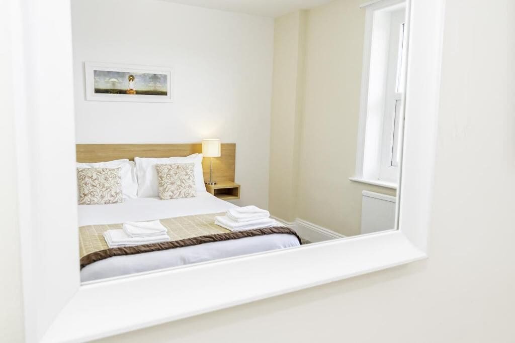 A hotel room with a bed, a nightstand, a lamp, a framed picture on the wall, and a window.