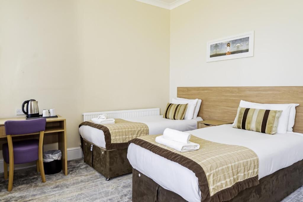 A hotel room with two beds, a desk, a chair, and a painting on the wall.