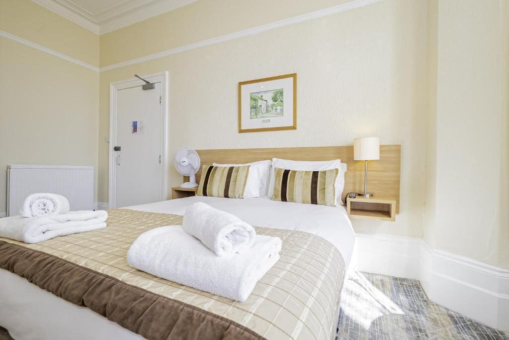 A hotel room with a large bed, a bedside table with a lamp, a framed picture on the wall, and a door with a handle.