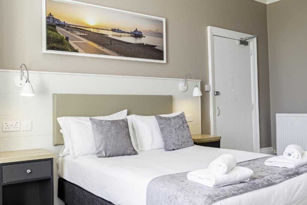 A neatly arranged hotel room with a bed, bedside tables, a framed picture on the wall, and a door.