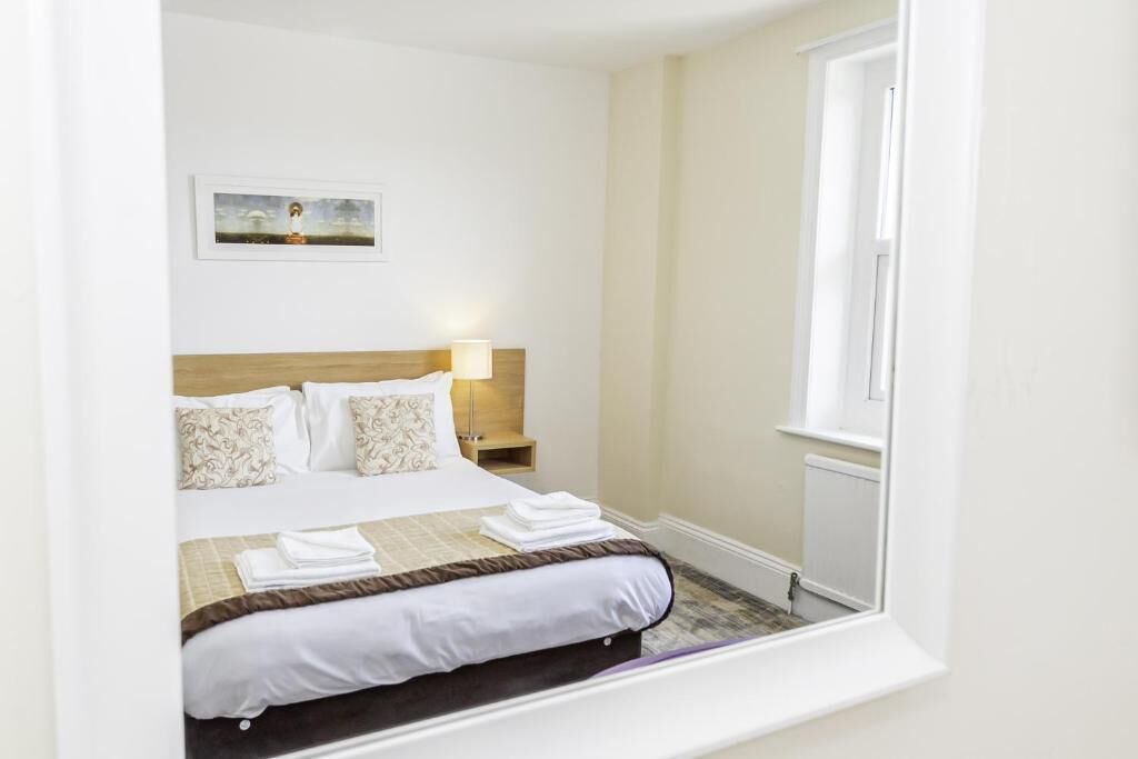 A hotel room with a bed, a nightstand, a lamp, and a framed picture on the wall.
