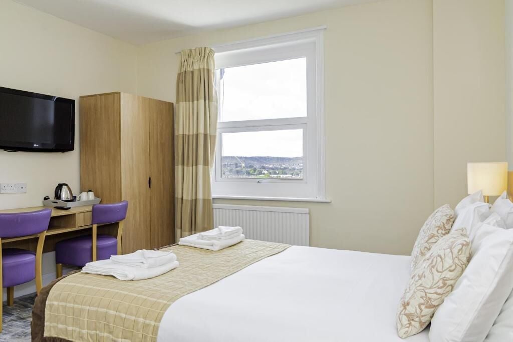 Hotelkamer met een bed, een aan de muur bevestigde televisie, een bureau met stoel, een raam met uitzicht en een radiator.
