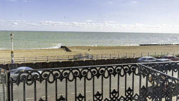 Une route côtière bordée d’une clôture métallique, une plage et une vue sur la mer.
