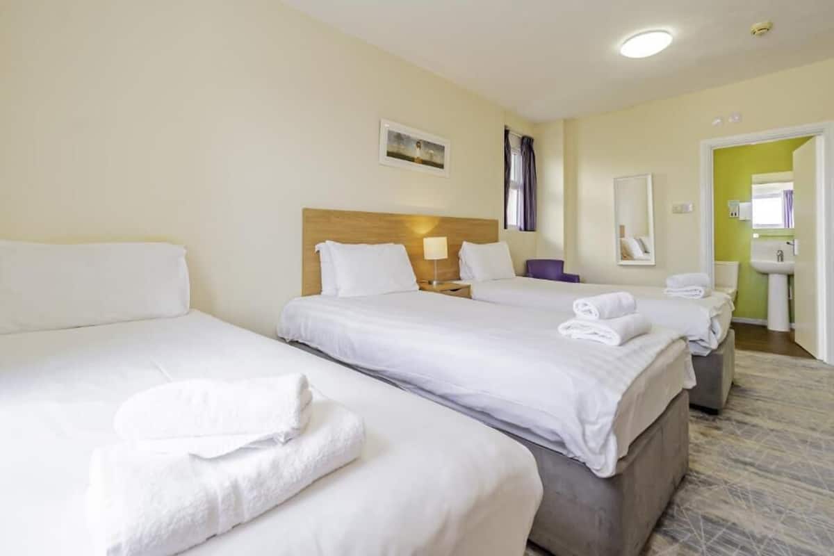 Een hotelkamer met twee bedden, een nachtkastje met een lamp, een spiegel en een badkamer die door een open deur zichtbaar is.