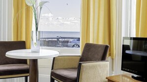 Une chambre d’hôtel avec vue sur la mer, une table ronde, deux chaises, un téléviseur et des rideaux jaunes.