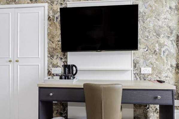 A modern room with a desk, a chair, a flat-screen TV mounted on the wall, and a coffee maker on the desk. - Majestic Hotel Eastbourne by Belvilla (Eastbourne)