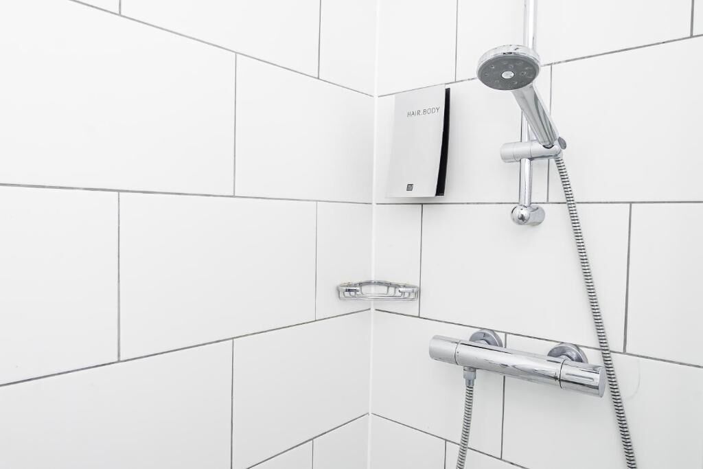 A modern bathroom with white tiles, a handheld showerhead, and a wall-mounted control panel.