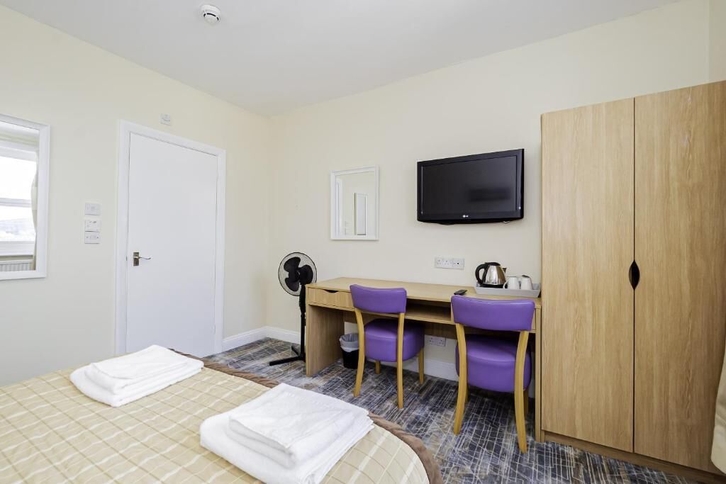 Una habitación de hotel con cama, escritorio con sillas, televisor y armario.