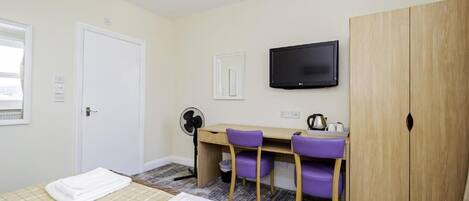 Una habitación de hotel con cama, escritorio con sillas, televisor y armario.