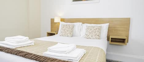 A neatly made bed with a brown accent, white linens, and a wooden headboard. There are two bedside tables with lamps, and a framed picture on the wall.