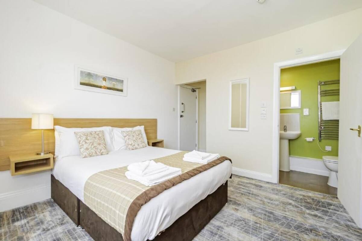 Een hotelkamer met een bed, een nachtkastje met een lamp, een schilderij aan de muur en een badkamer met een groene muur en een handdoekhouder.