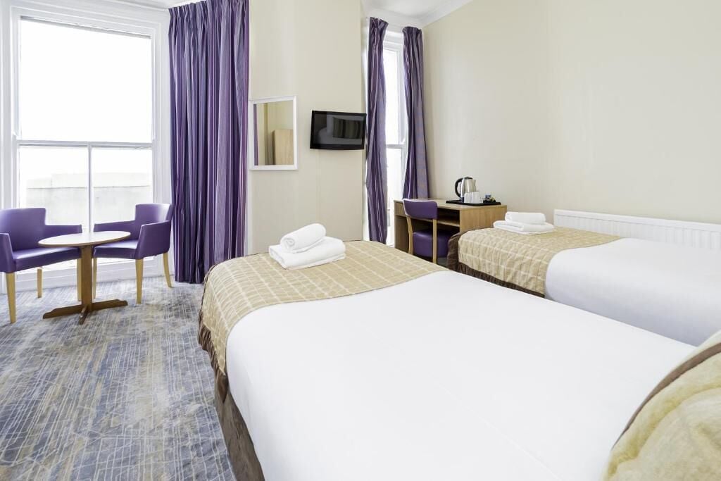 A hotel room with two beds, a desk, a chair, and a television.