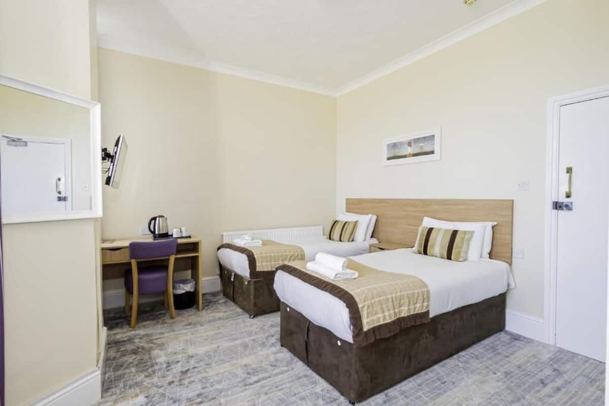 Hotelkamer met twee bedden, een bureau, een stoel en een tafeltje met een waterkoker.