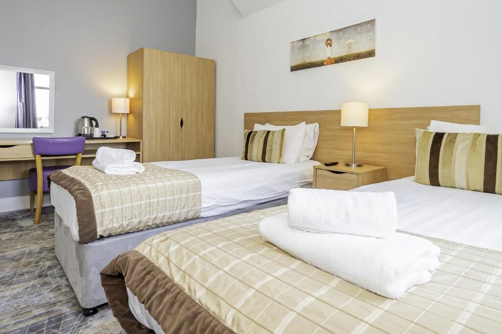 A hotel room with two beds, a desk, a chair, and a painting on the wall.