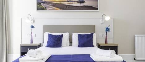 A neatly made bed with white and blue bedding, two bedside tables with lamps, and a framed picture above the bed.