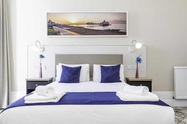 A neatly made bed with white and blue bedding, two bedside tables with lamps, and a framed picture above the bed. - Majestic Hotel Eastbourne by Belvilla (Eastbourne)