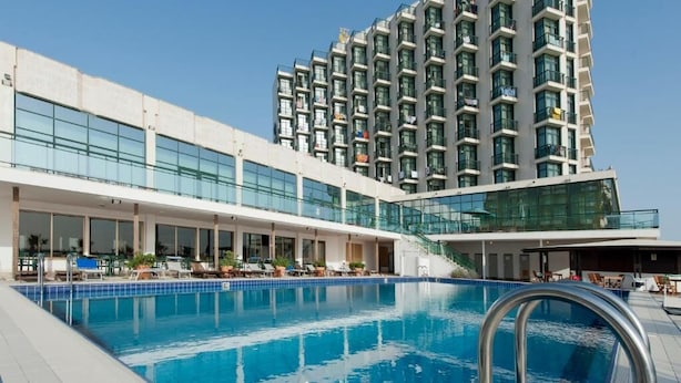 Un hotel moderno con piscina, varios balcones y fachada de vidrio.