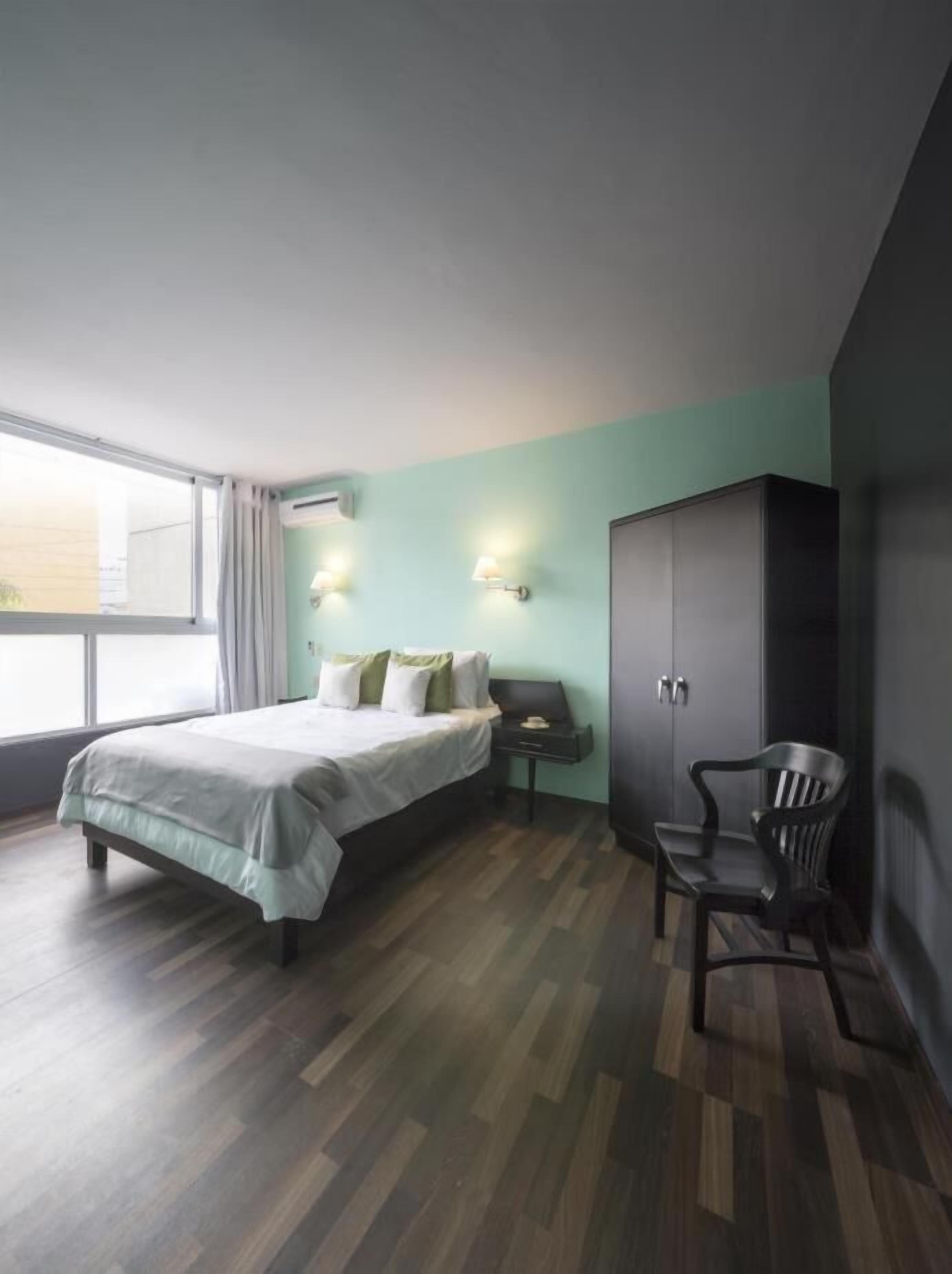 Un dormitorio con cama, armario, silla y mesita de noche.