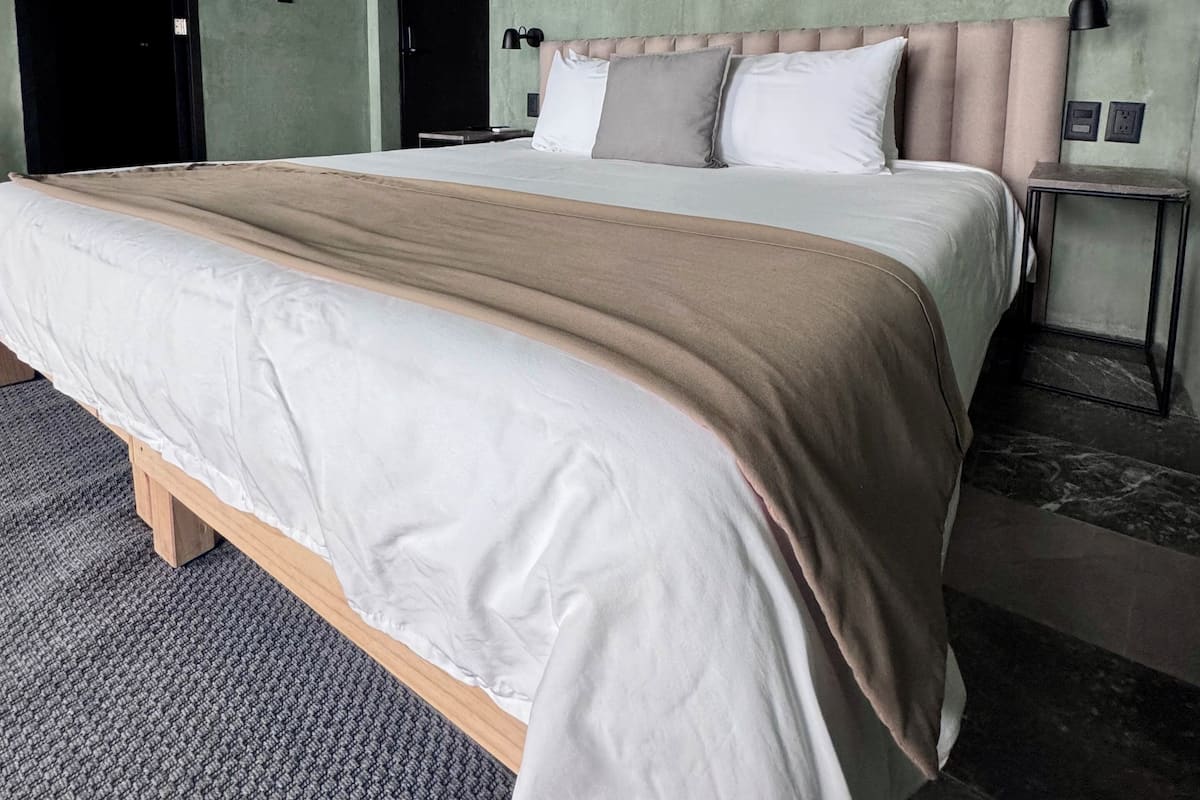 Een moderne slaapkamer met een groot bed, een hoofdeinde, een nachtkastje en een lijst met een afbeelding aan de muur.