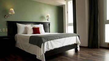 Ein ordentlich gemachtes Bett mit weißer und grauer Bettwäsche, zwei Wandlampen und ein großes Fenster mit Vorhängen.