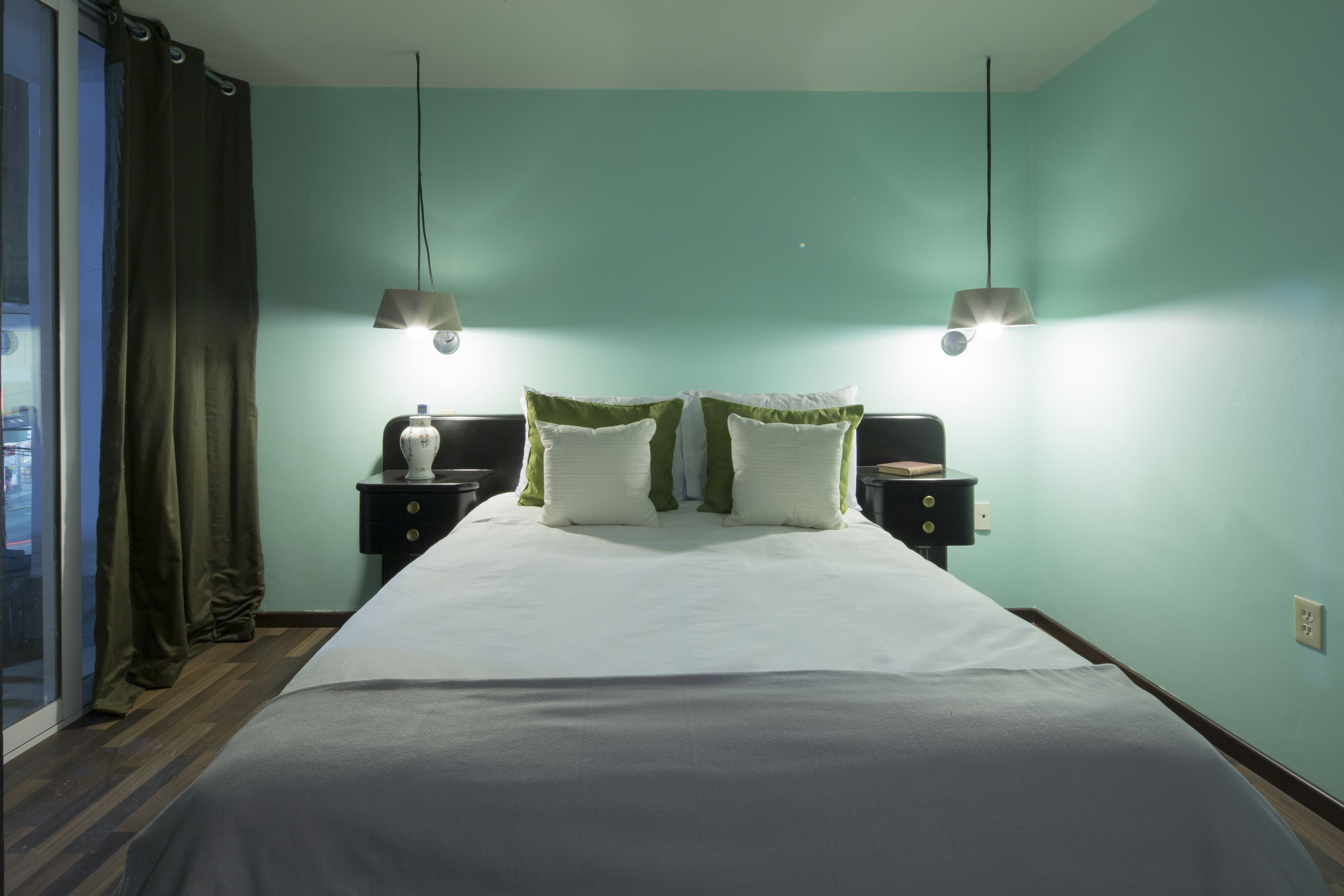 A hotel room with a large bed, two bedside tables, and a view through a window with curtains.