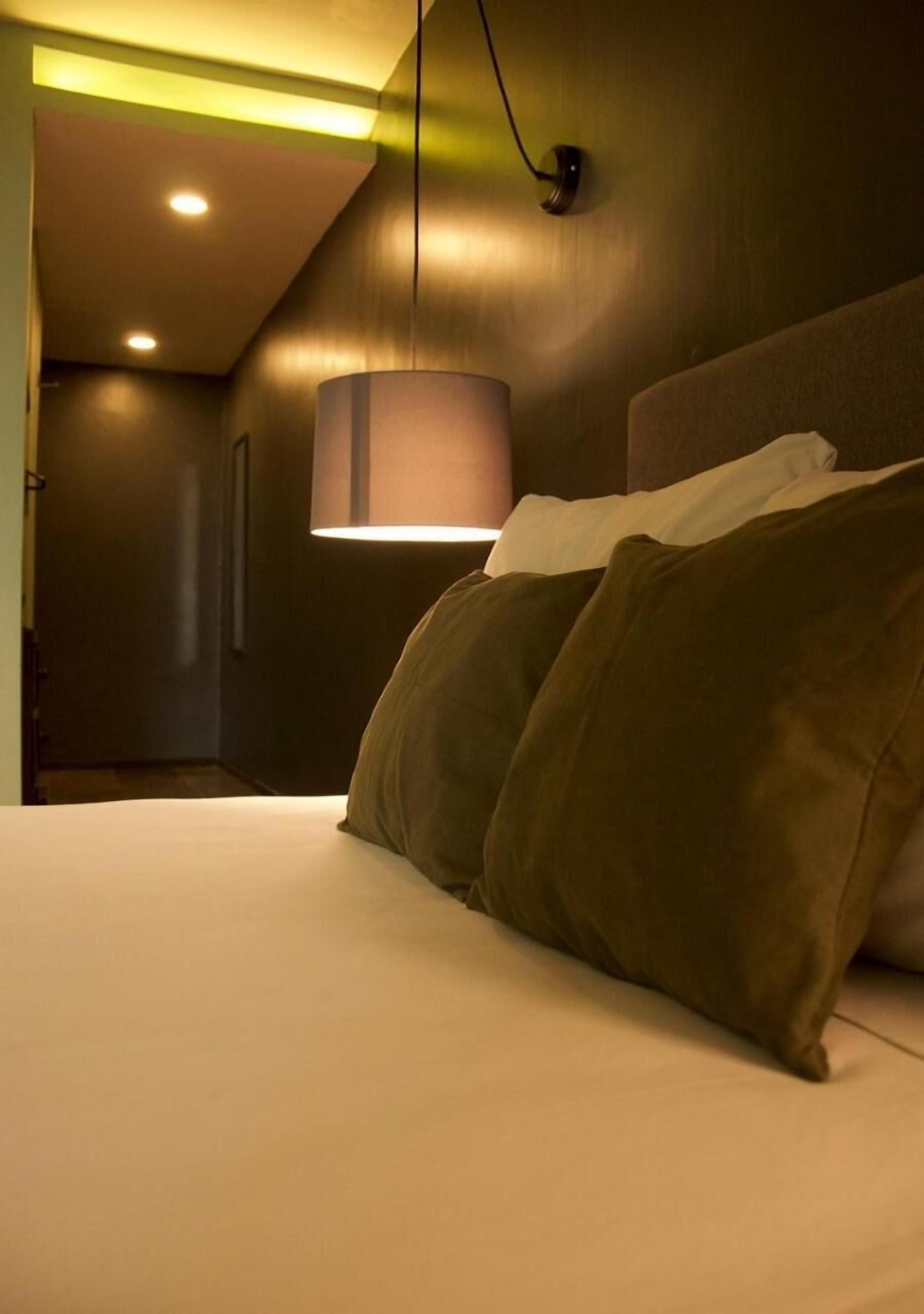 A hotel room with a bed, a wall-mounted lamp, and a ceiling light.
