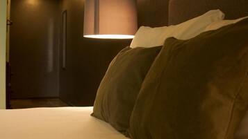 A hotel room with a bed, a wall-mounted lamp, and a ceiling light.