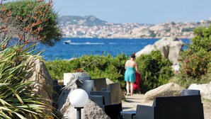 A coastal view with a pathway, rocks, and a distant town. - Club Esse Residence Capo D'orso (Palau)