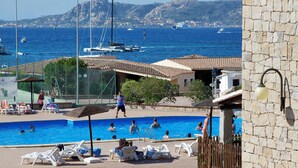A swimming pool with lounge chairs, a view of the sea, and a stone wall. - Club Esse Residence Capo D'orso (Palau)