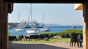 A view of a marina with boats, outdoor seating, and a stone building structure. - Club Esse Residence Capo D'orso (Palau)