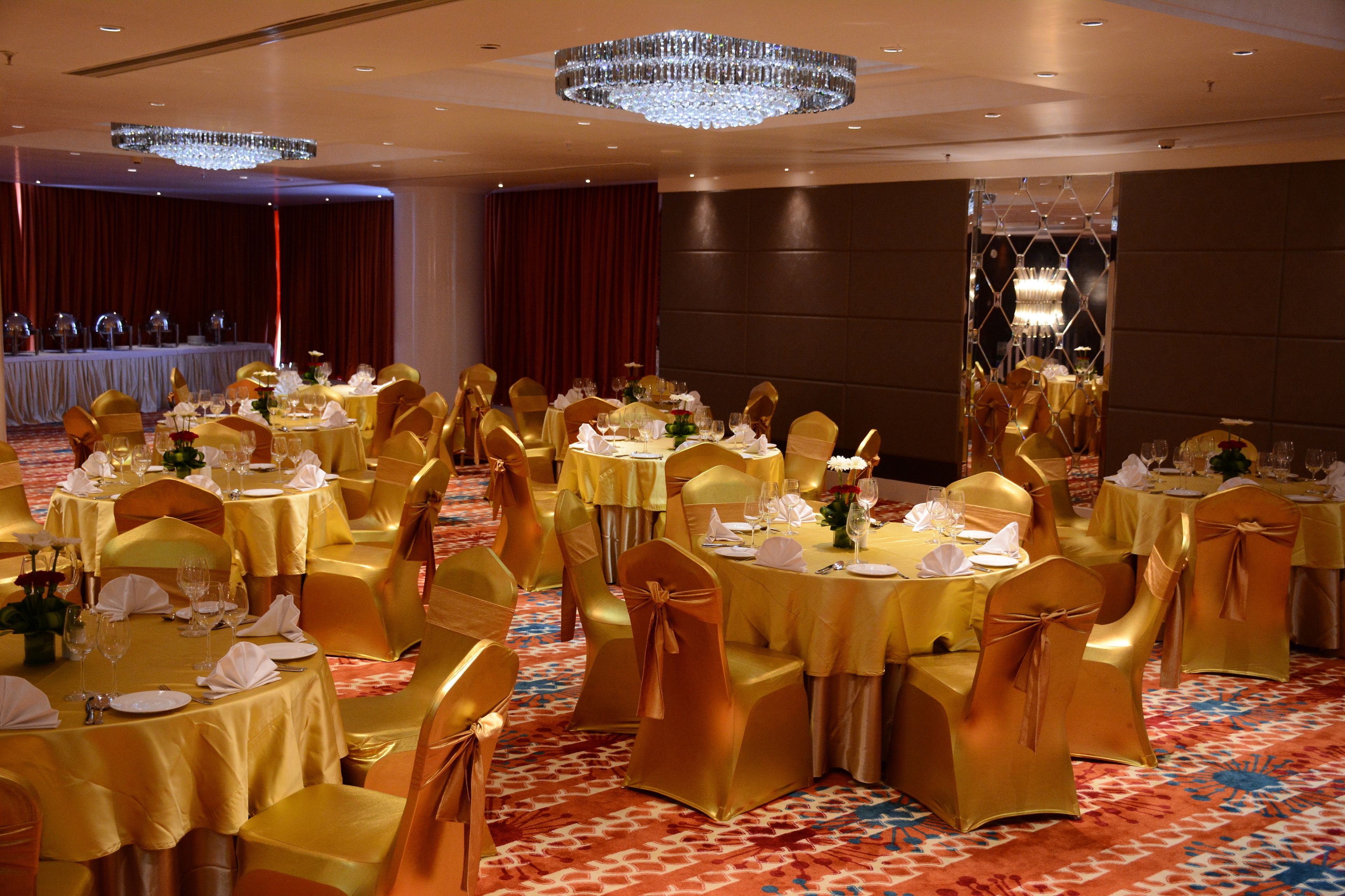 Un salón de banquetes con mesas redondas, sillas doradas y una alfombra con diseño.