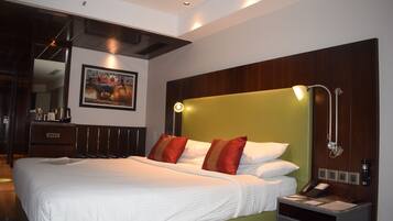A hotel room with a large bed, a bedside table with a phone and papers, and a wall-mounted lamp.