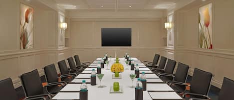 A conference room with a long table, chairs, water bottles, and a large screen on the wall.