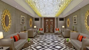 Un hall d’entrée spacieux doté d’un sol à motifs géométriques, de deux canapés avec des coussins rouges et d’un grand plafond décoratif.