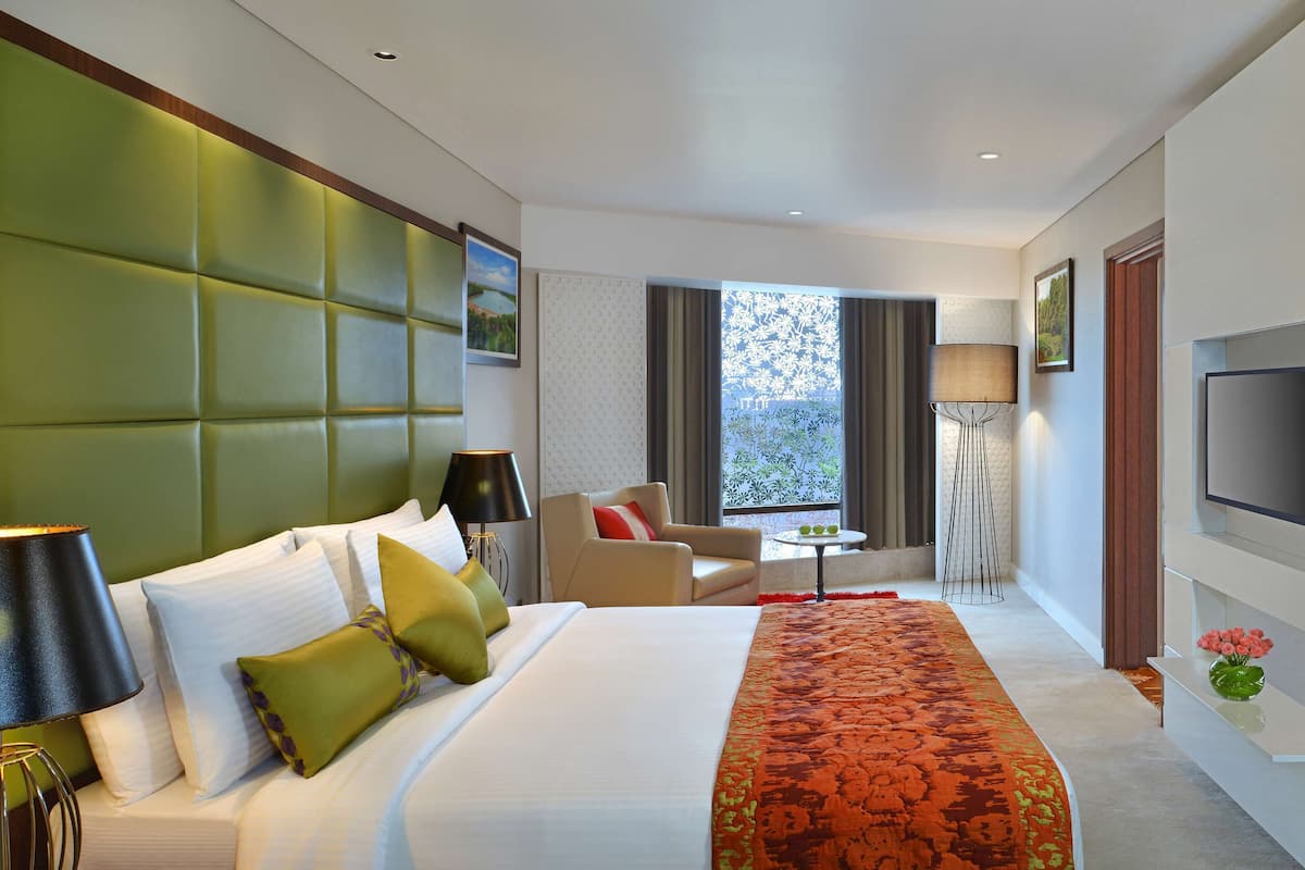 A hotel room with a large bed, a sofa, a TV, and a window with a view.