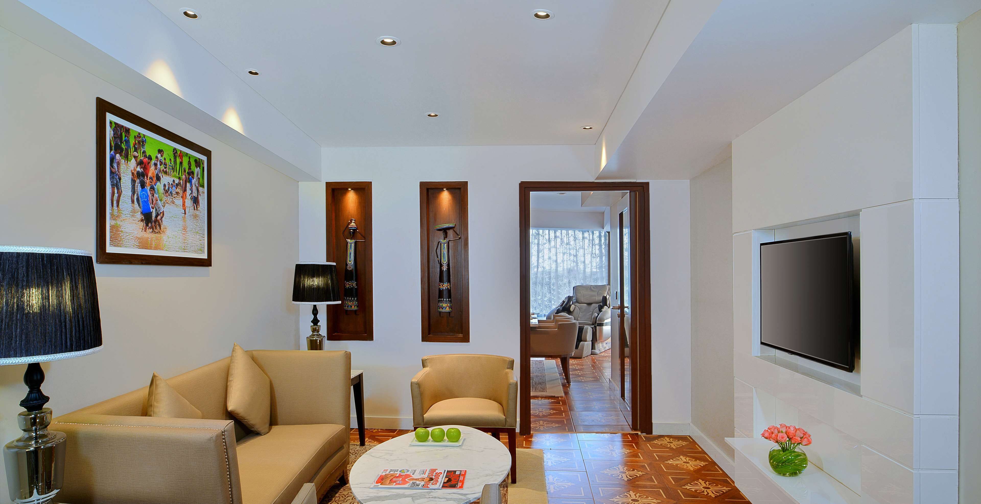 A modern hotel room with a sofa, a coffee table with magazines, a TV, and a painting on the wall.