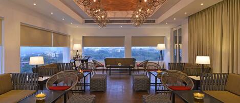 A spacious hotel lobby with a modern chandelier, comfortable seating, and large windows offering a city view.