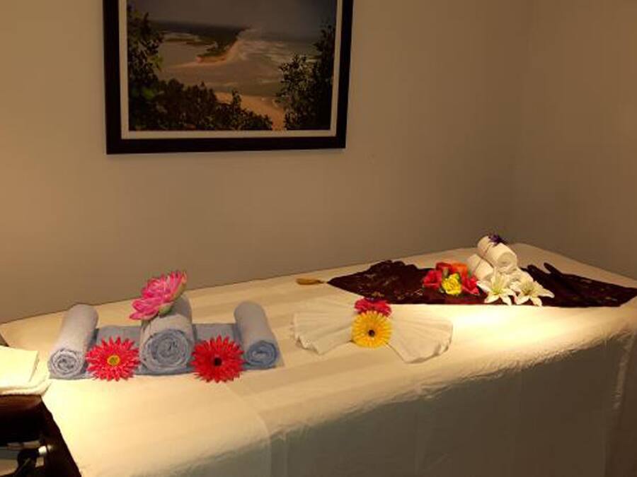 Une table de massage avec des serviettes, des fleurs et une serviette enroulée.
