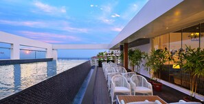 A rooftop pool area with a view of the ocean, white wicker chairs, and potted plants. - Country Inn & Suites by Radisson, Manipal (Udupi)