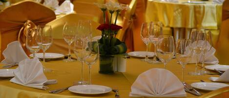 A banquet hall with tables set for a formal event, featuring white tablecloths, gold chairs, and empty wine glasses.