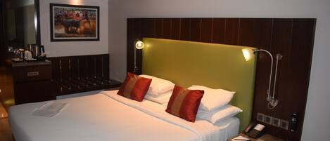 A hotel room with a large bed, a bedside table with a phone and papers, a mirror, and a picture on the wall.