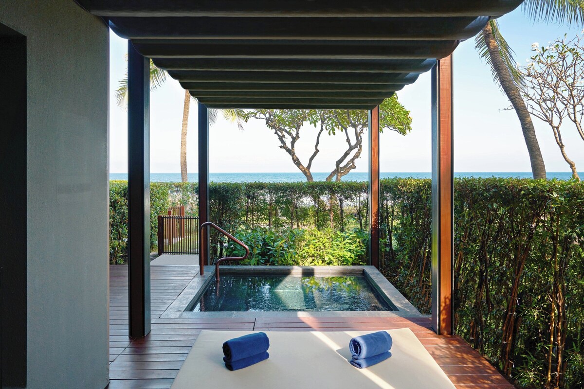 Un espace piscine privé avec une terrasse en bois, deux chaises longues et une vue sur la mer et les arbres.