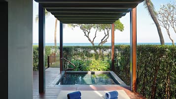 A private pool area with wooden deck, two lounge chairs, and a view of the sea and trees.