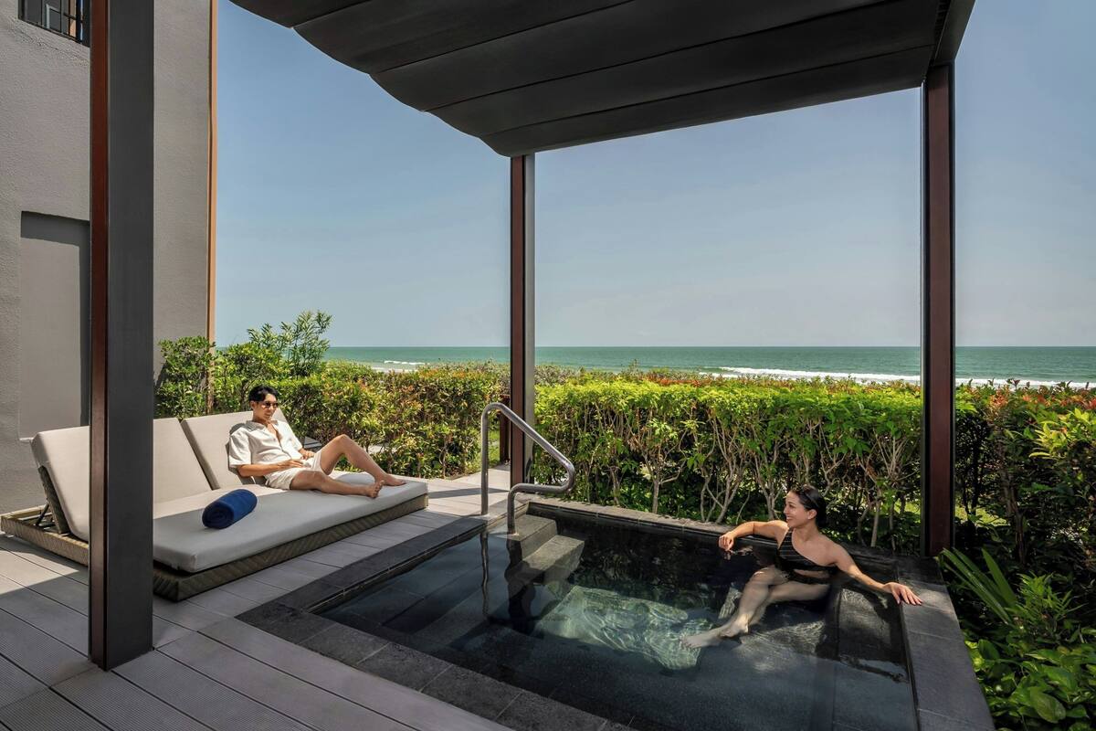 Een modern buitenzwembad met een glazen hottub, een ligstoel en uitzicht op de oceaan.